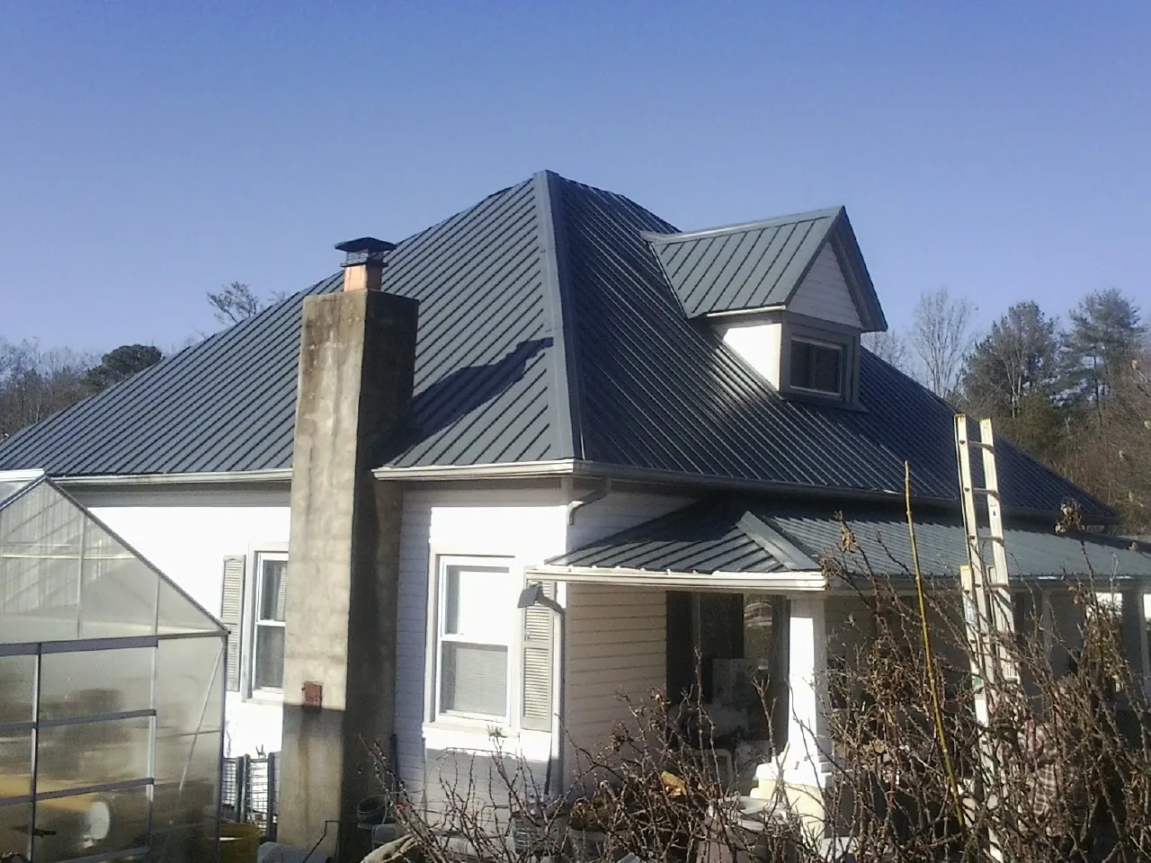 Dark blue standing seam metal roof on a white farmhouse with dormer — Slate & Tile Roof Repair by Roofing Brothers in Milwaukee