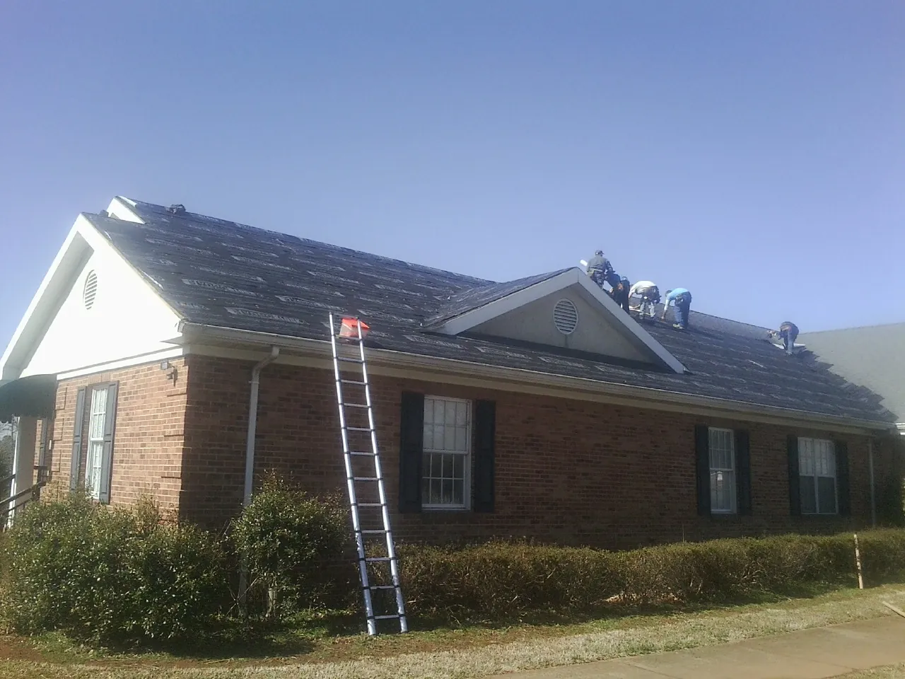 Crew tearing shingles off a brick ranch roof with a ladder set — Emergency Roof Repair work by our crew in Milwaukee