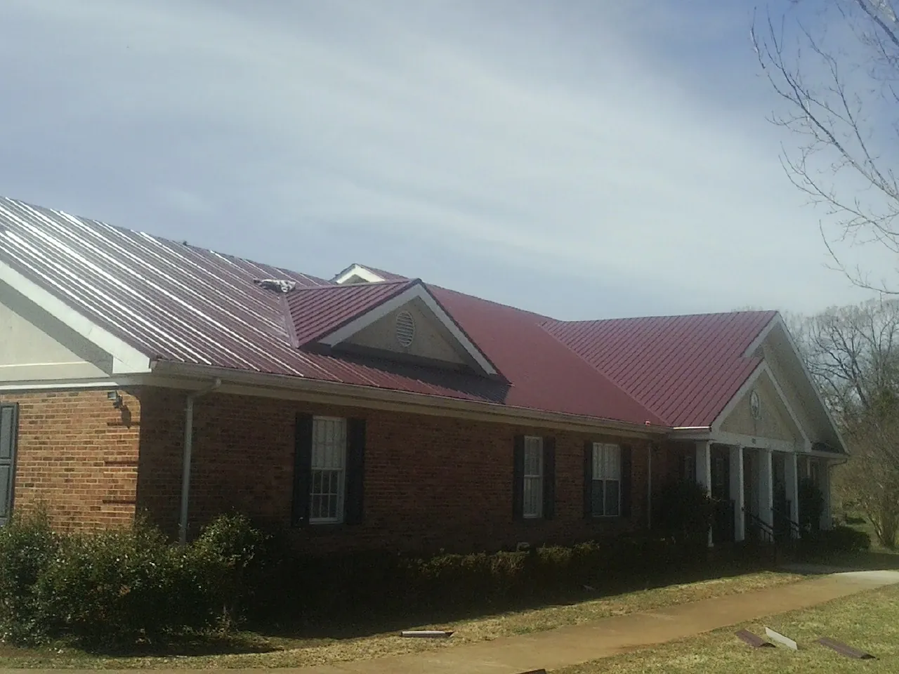 Red metal roof with gabled entries on a long brick building, from a Hail Damage Roof Repair job in Milwaukee