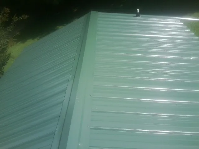 New green metal panels meeting at the ridge of a roof — Flat Roof Repair work by our crew in Milwaukee