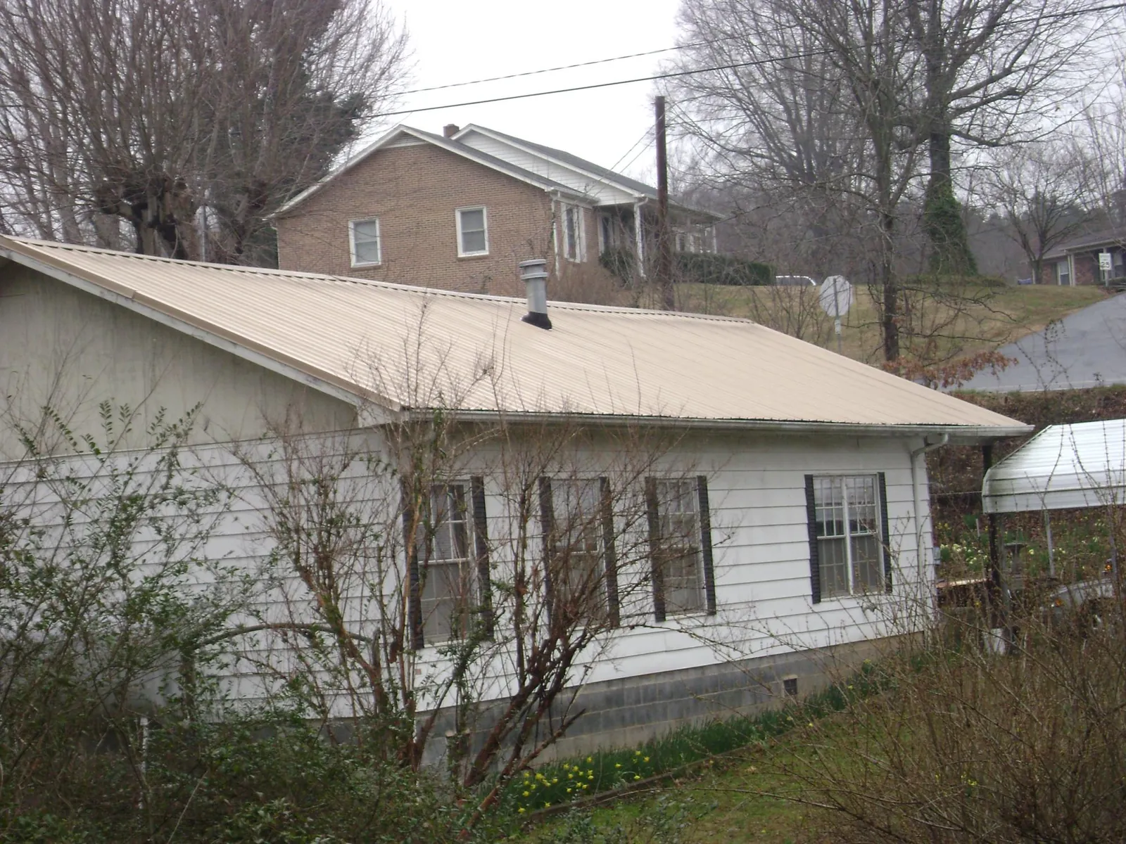 Tan metal roof on a white sided house set into a hillside — Commercial Roofing by Roofing Brothers in Milwaukee